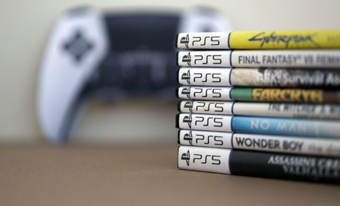 A stack of physical PS5 games with a controller in the background